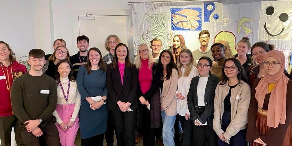 A group of young people stand in a conference room in front of a fabric mural.