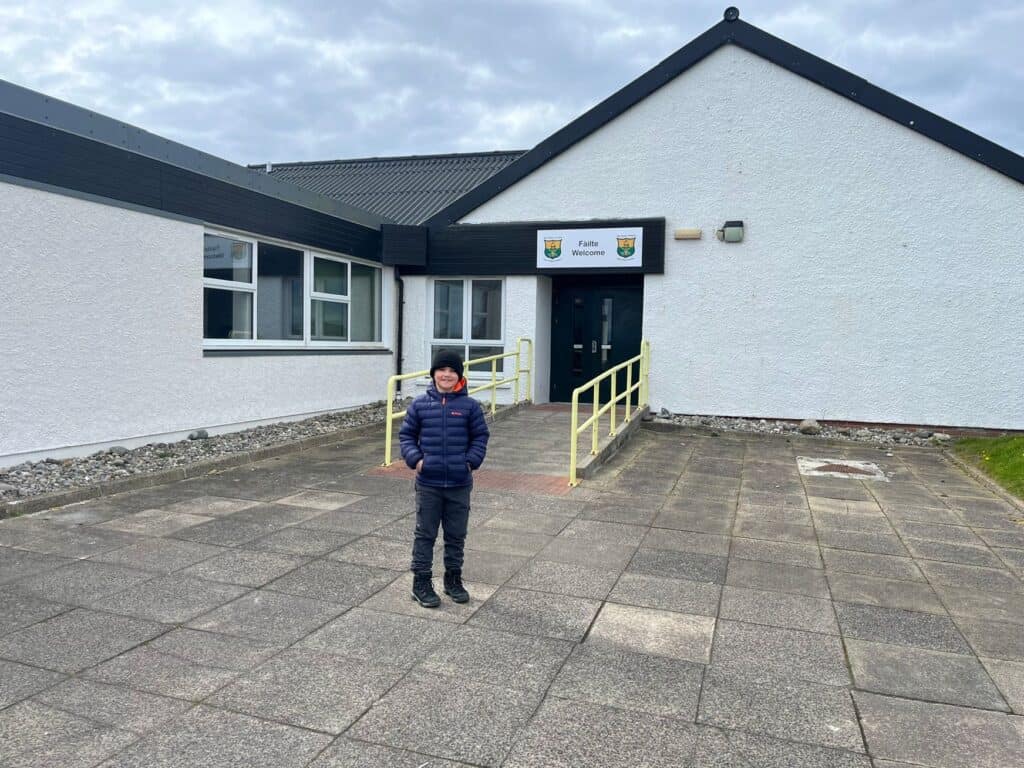 A boy standing hands in pocket in front of a school building.